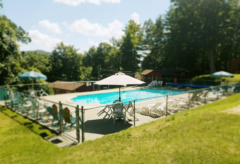 Swimming pool surrounded by lounge chairs and umbrellas, set in a serene outdoor space with trees in the background, ideal for relaxation.